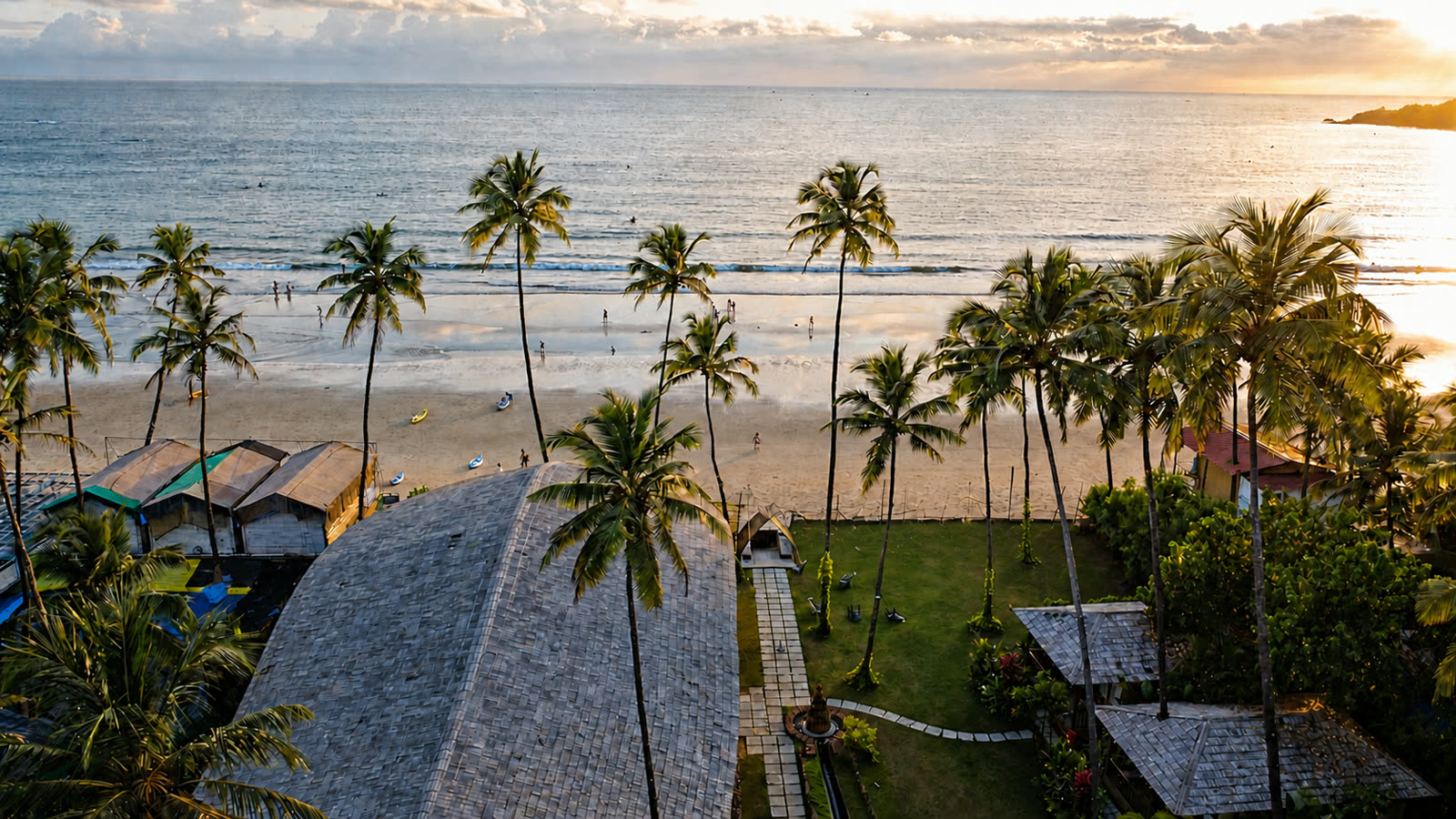 Aerial view of The Wave Goa's tropical garden opening onto Palolem Beach at sunset
