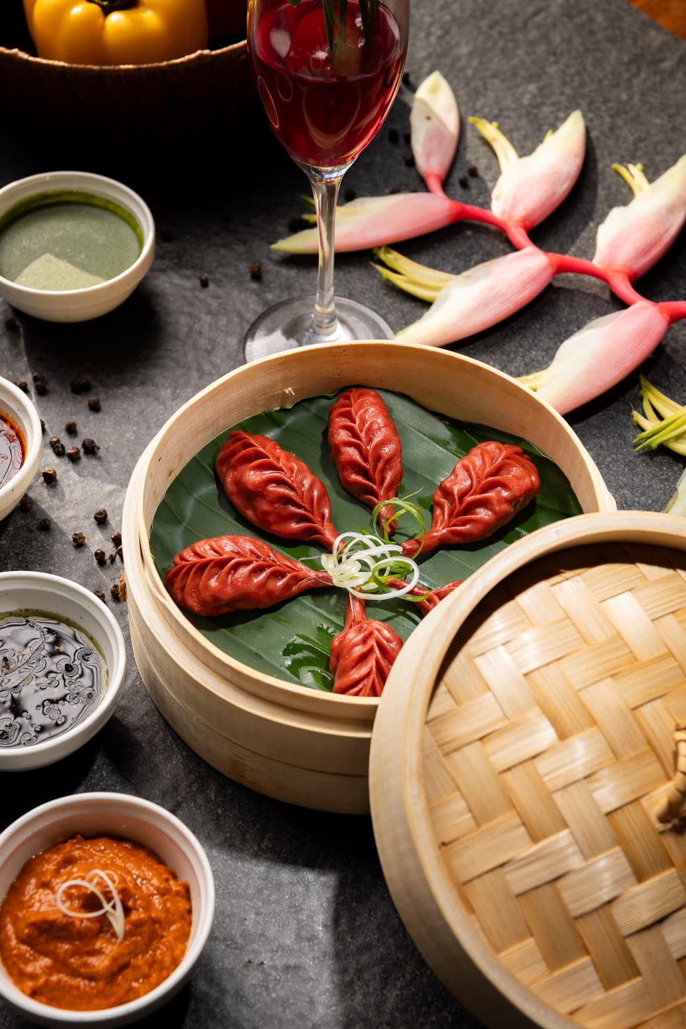 Red momos arranged in a bamboo steamer with dipping sauces