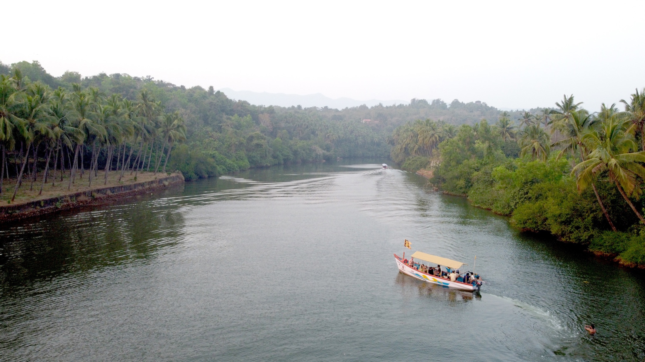 A passenger boat gliding through a palm-lined river in South Goa